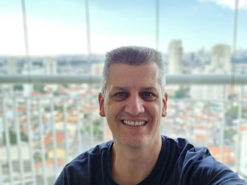 Foto do Robson em frente a uma janela com vista para a cidade.